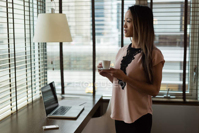 Empresária desviando o olhar enquanto toma café no escritório — Fotografia de Stock