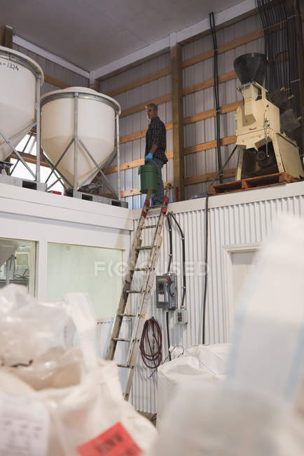 Man standing with bucket near grain elevator in factory — Stock Photo
