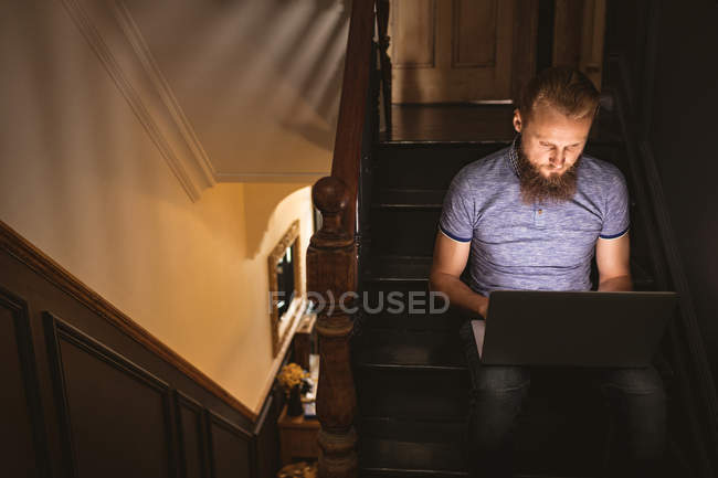 Mann benutzt seinen Laptop, während er zu Hause im Treppenhaus sitzt — Stockfoto