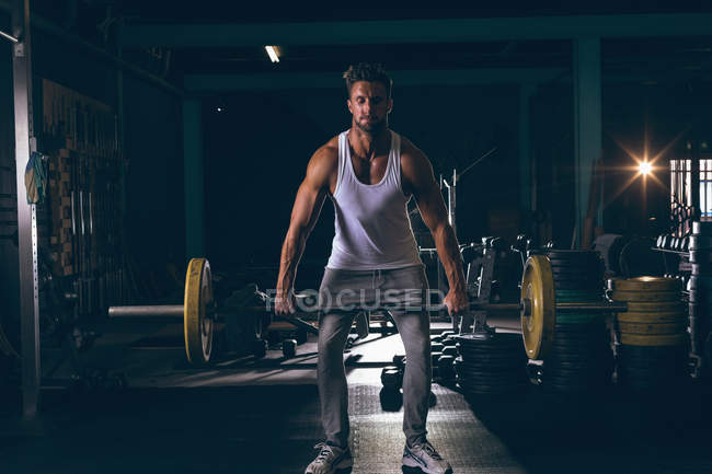 Retrato de un hombre musculoso haciendo ejercicio con barra en el gimnasio - foto de stock