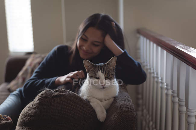 Teenage girl sitting with cat on sofa in living room at home — Stock Photo