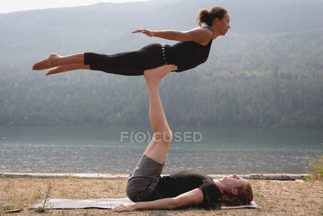 Спортивна пара практикує акро-йогу біля узбережжя моря в сонячний день — стокове фото