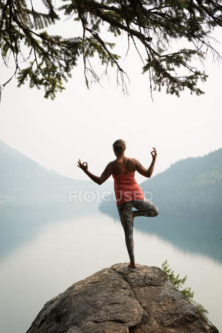 Mujer en forma de equilibrio en una pierna en el borde de una roca a la hora del amanecer - foto de stock