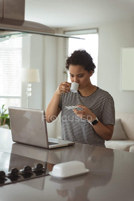 Donna che prende il caffè mentre lavora sul computer portatile a casa — Foto stock