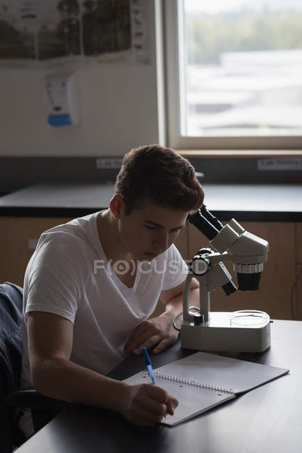 Teenage boy experimenting on microscope in laboratory at university — Stock Photo