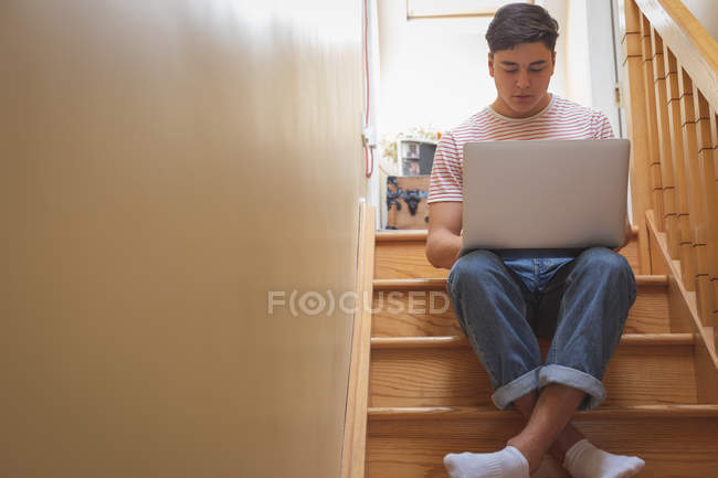Uomo che utilizza il computer portatile su scale in legno a casa
. — Foto stock