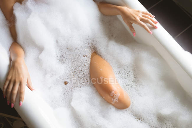 Vue recadrée de la femme prenant un bain avec de la mousse dans la baignoire à la maison . — Photo de stock