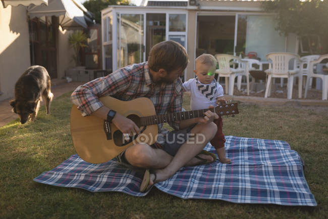 Отец играет на гитаре с сыном в саду в солнечный день — стоковое фото