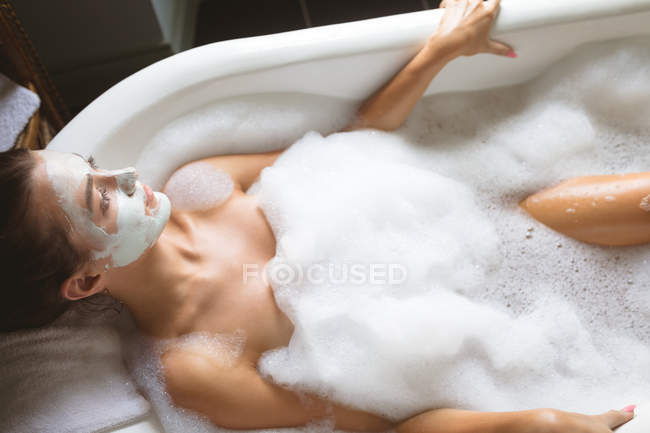 Mulher com máscara facial relaxante em espuma na banheira em casa . — Fotografia de Stock