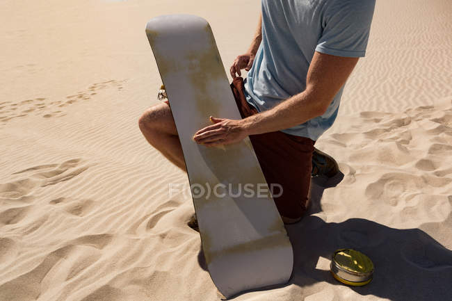 Mann trägt an einem sonnigen Tag Surfbrettwachs auf Sandbrett in der Wüste auf — Stockfoto
