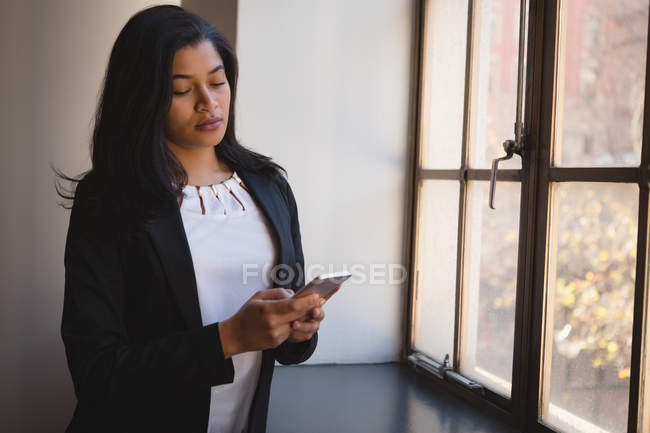 Donna d'affari che utilizza il telefono cellulare vicino alla finestra in ufficio . — Foto stock