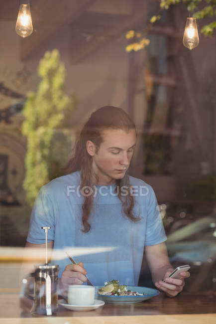 Человек, использующий мобильный телефон во время завтрака в кафе — стоковое фото
