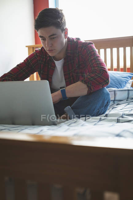 Молодий чоловік працює з ноутбуком, сидячи на ліжку . — стокове фото