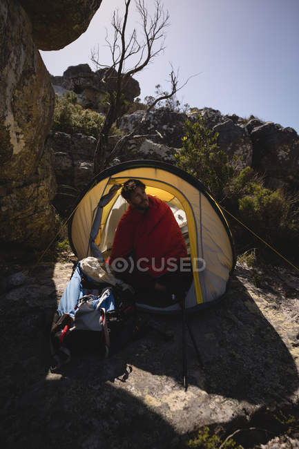 Турист, завернутый в одеяло, сидит в палатке в солнечный день — стоковое фото