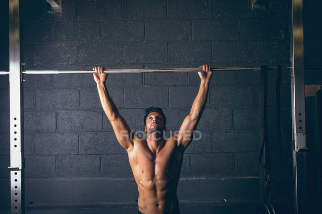 Мускулистый мужчина тренируется на подтягивающем баре в фитнес-студии — стоковое фото