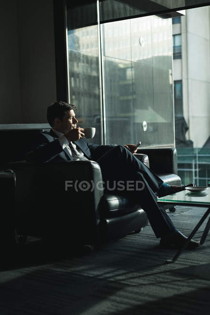 Empresário atencioso usando telefone celular enquanto toma café no lobby do hotel — Fotografia de Stock