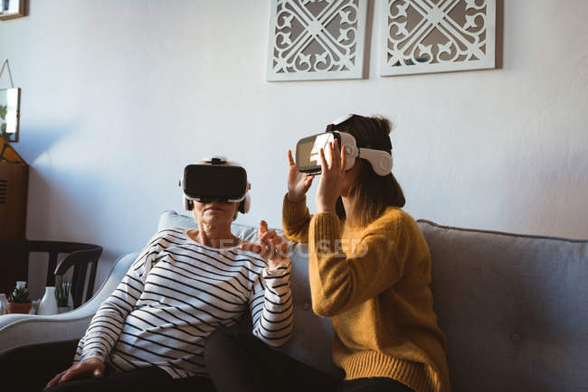 Seniorin und Tochter tragen ein Virtual-Reality-Headset, während sie sich auf einem Sofa entspannen — Stockfoto