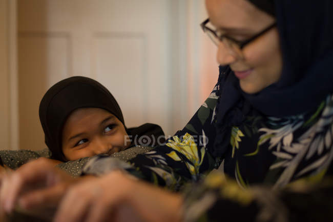 Madre e hija musulmanas sonriendo en casa - foto de stock