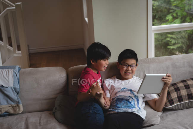 Frères et sœurs utilisant une tablette numérique dans le salon à la maison — Photo de stock