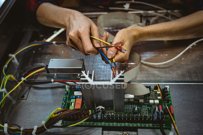 Trabajadora sujetando un cable en la placa de circuito en fábrica - foto de stock