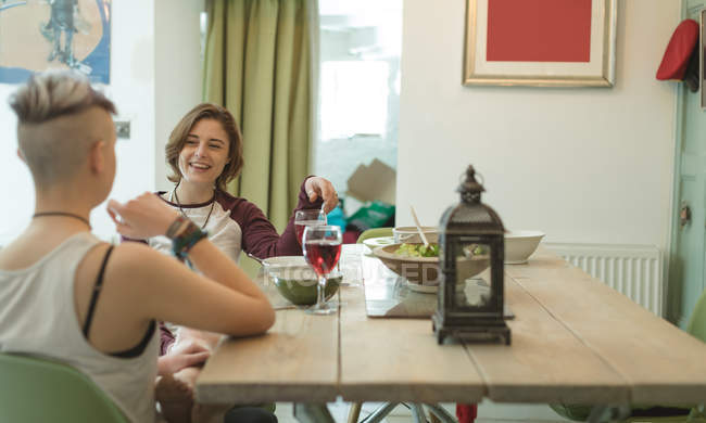 Couple lesbien dînant avec des verres de vin rouge dans le salon moderne
. — Photo de stock