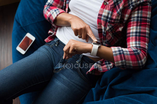 Female executive sitting on arm chair and using smartwatch in office — Stock Photo