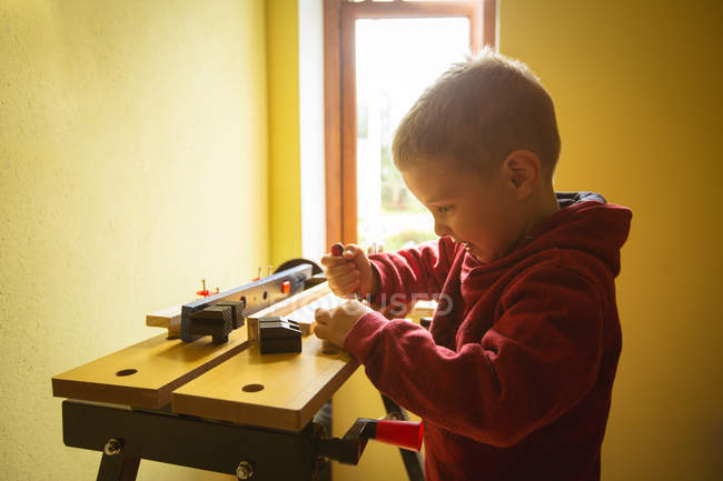 Menino usando ferramenta na prancha de madeira em casa — Fotografia de Stock
