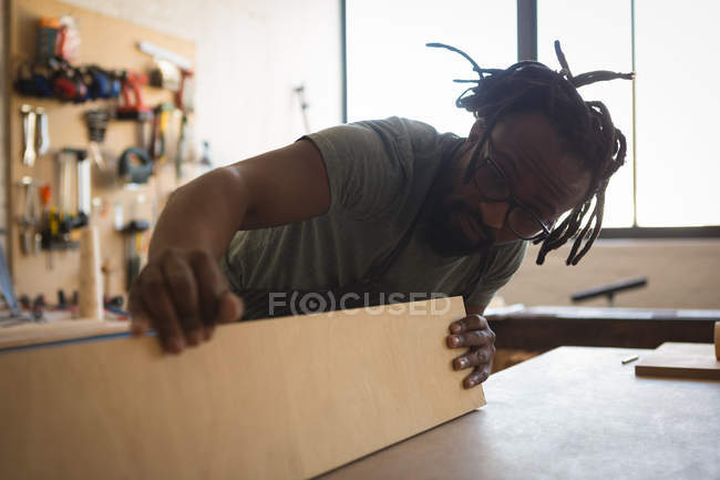 Carpenter looking at wooden plank in workshop — Stock Photo