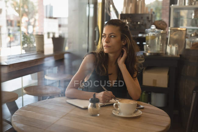 Mujer pensativa escribiendo en el diario en la cafetería - foto de stock