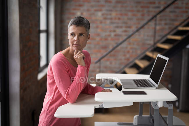 Ejecutivo femenino reflexivo usando el ordenador portátil en la oficina . - foto de stock