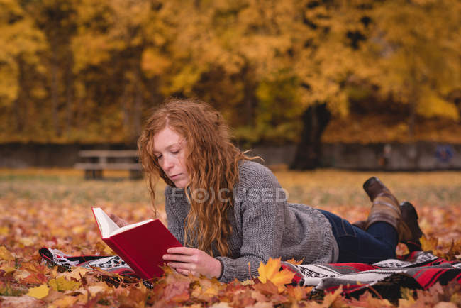 Красива жінка лежить в осінньому парку і читає книгу — стокове фото