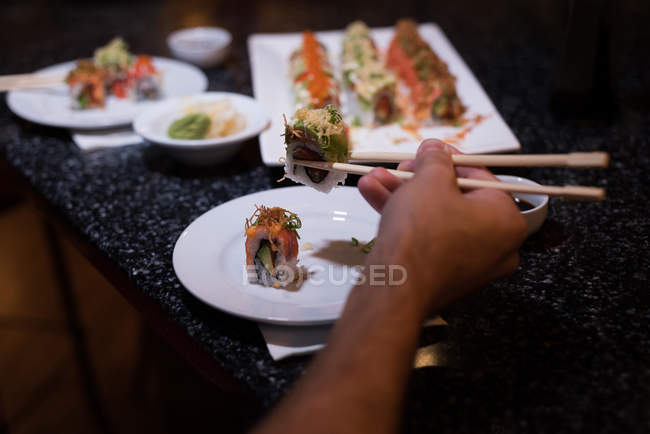 Uomo che raccoglie sushi con le bacchette in un ristorante — Foto stock