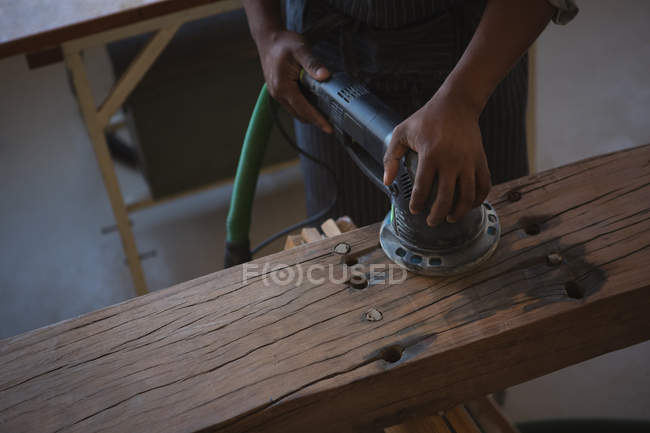 Sección media de madera de nivelación de carpintero con pulidora en taller - foto de stock
