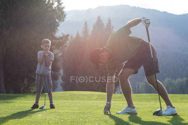 Padre ajustando pelota de golf en tee en el campo - foto de stock
