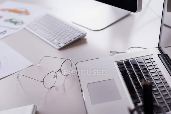 Close-up of laptop, computer keyword, spectacles and documents on office table — Stock Photo
