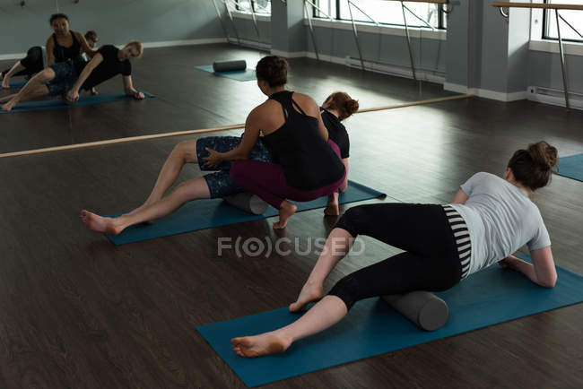 Treinador auxiliando as pessoas na prática de ioga no estúdio de fitness . — Fotografia de Stock