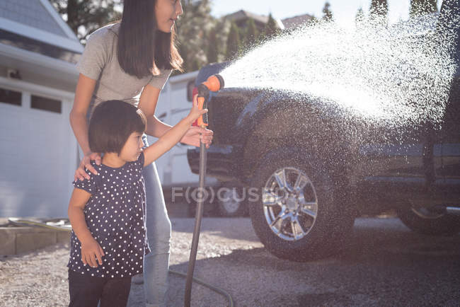 Mère et fille laver une voiture avec un jet d'eau haute pression par une journée ensoleillée — Photo de stock