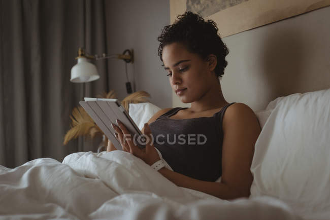 Женщина с помощью цифрового планшета на кровати в спальне — стоковое фото