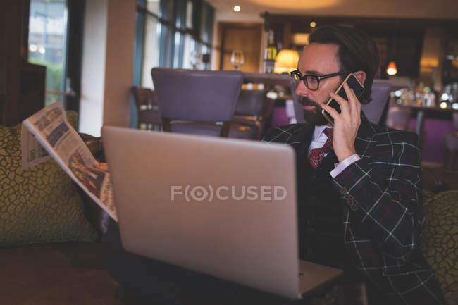 Empresário pegando celular enquanto lia jornal no hotel — Fotografia de Stock