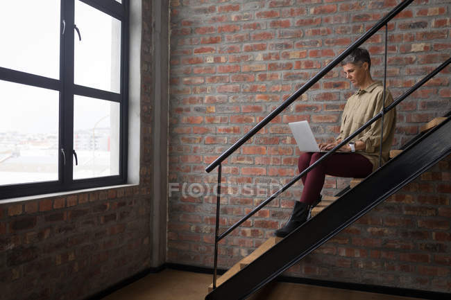 Empresaria usando laptop en escaleras en la oficina . - foto de stock