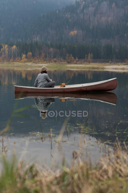 Man and his pet dog sitting on boat in silent river — Stock Photo