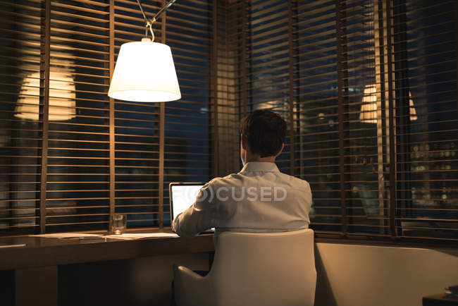 Rear view of businessman using laptop at desk in hotel — Stock Photo