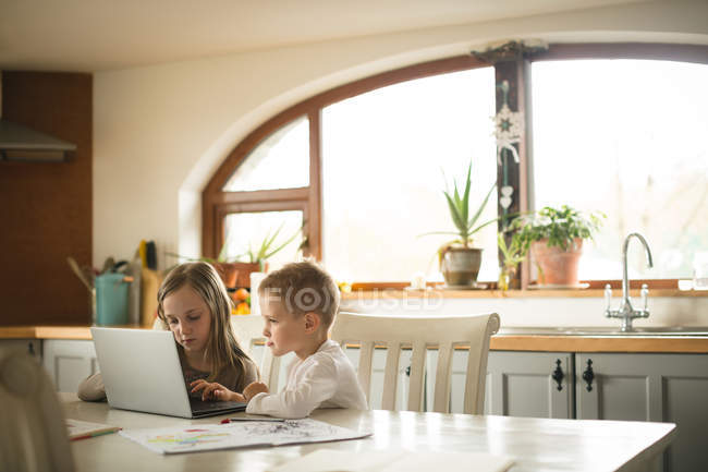 Bambini che usano il computer portatile insieme in cucina a casa — Foto stock
