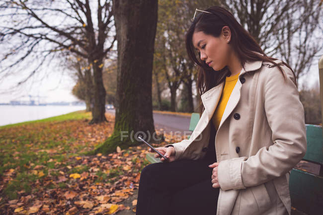 Деловая женщина, сидя на скамейке запасных осенью, пользуется мобильным телефоном — стоковое фото