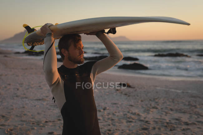 Surfeur portant une planche de surf sur la tête à la plage — Photo de stock