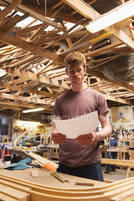 Junger Tischlermeister schaut in Werkstatt auf Schaubild — Stockfoto