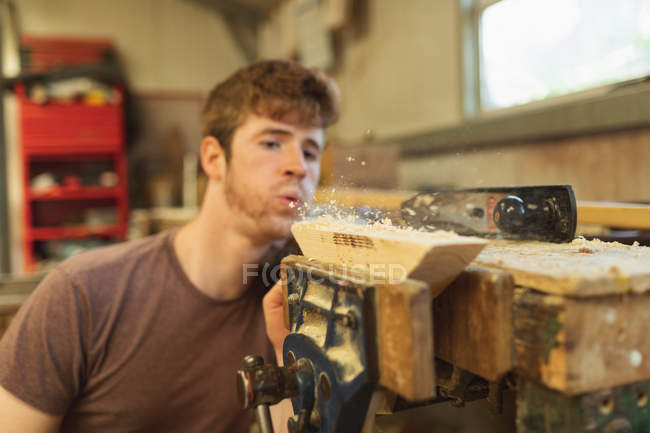 Junger Tischler bläst in Werkstatt Holzspäne — Stockfoto