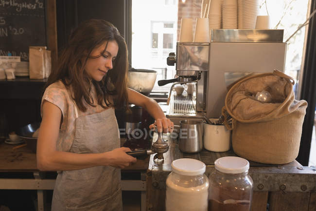 Barista usando uma adulteração para pressionar café moído em um portafilter no café — Fotografia de Stock