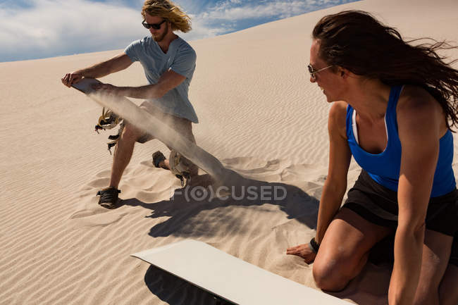 Pareja revisando sandboard en duna de arena en el desierto - foto de stock