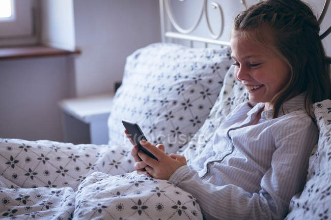 Girl using mobile phone on bed in bedroom — Stock Photo